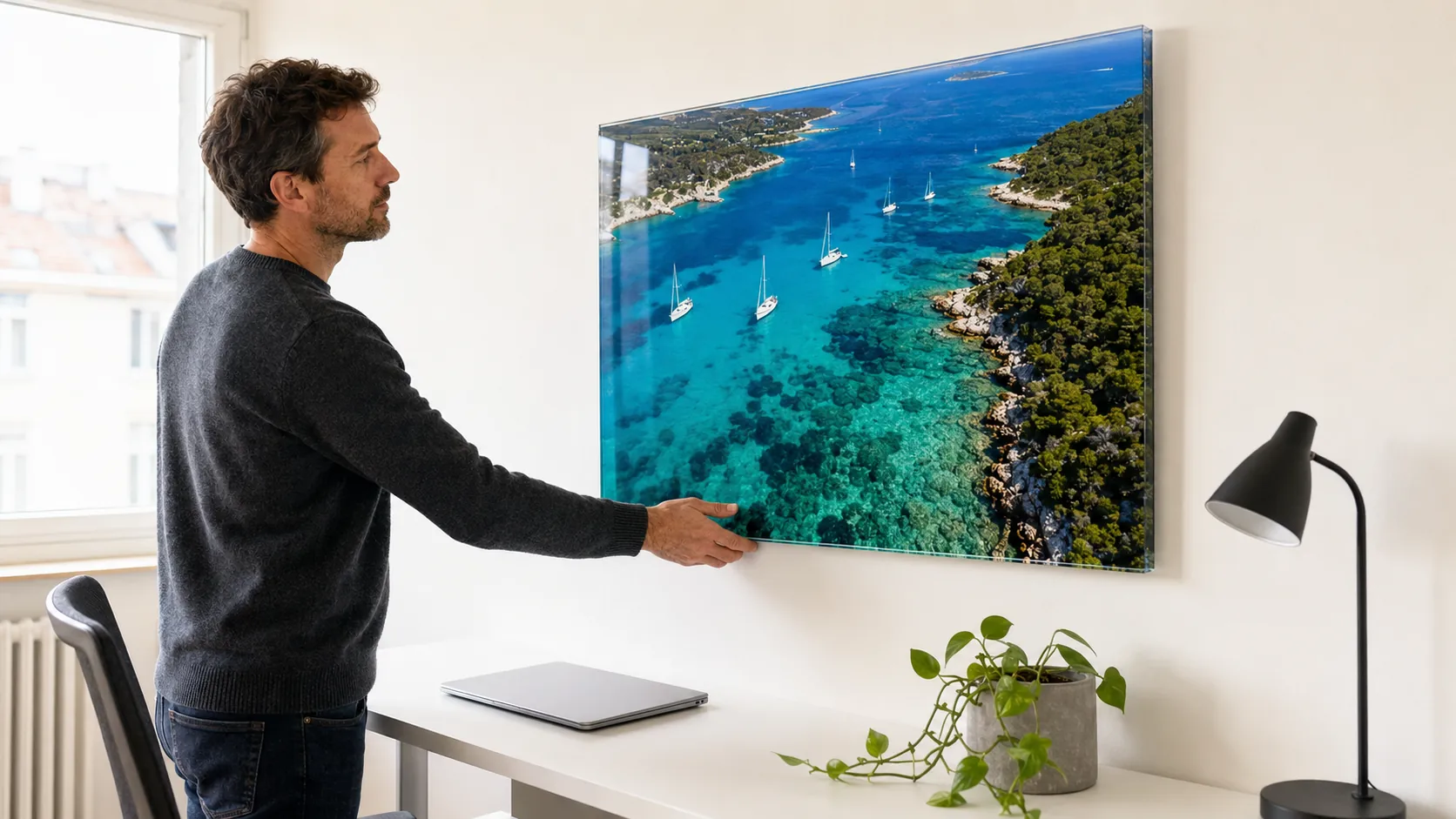 Mann hängt ein Foto einer türkisen Bucht hinter Acrylglas im Büro auf