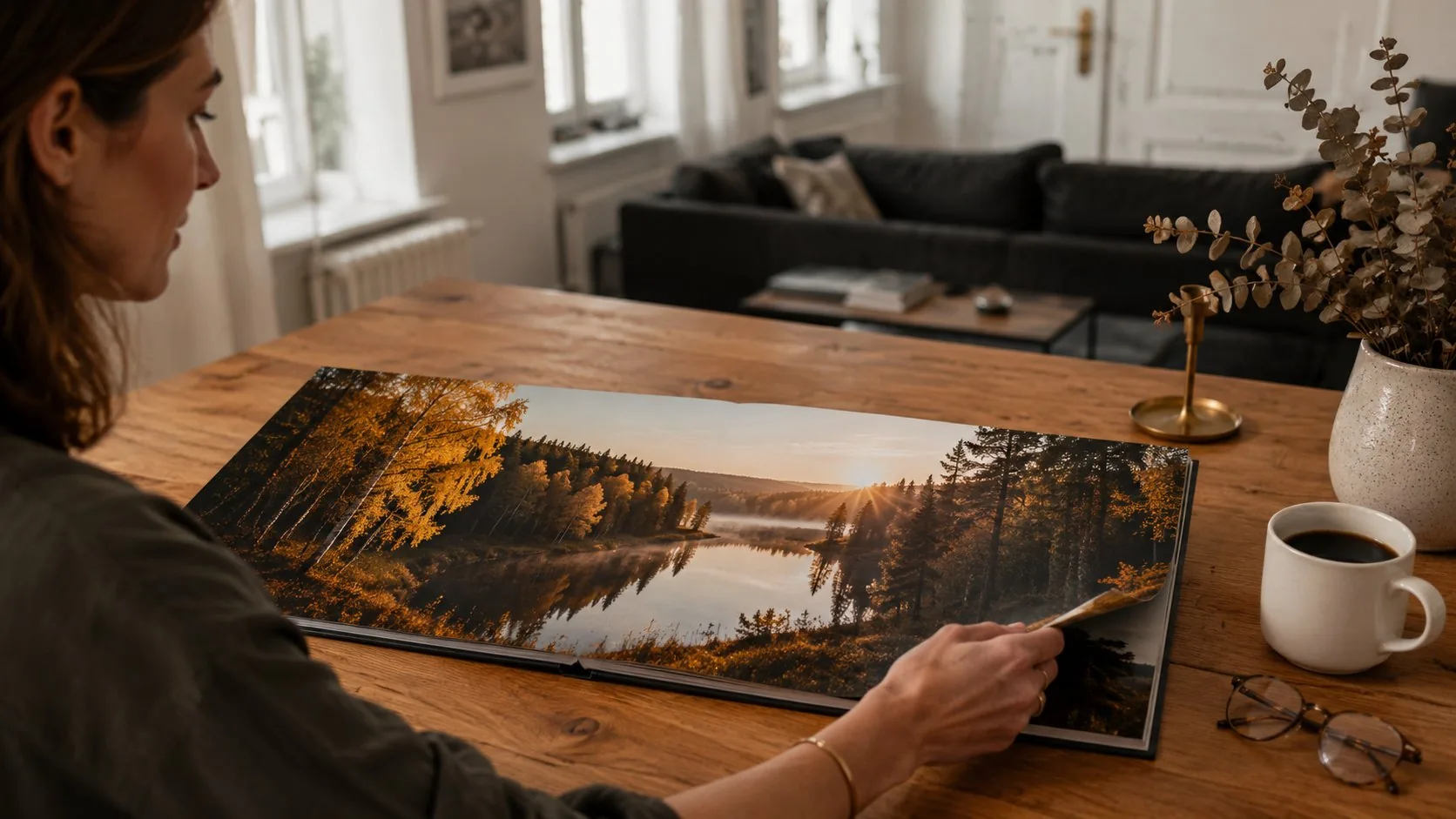 Frau betrachtet ein aufgeschlagenes Layflat Fotobuch mit Panorama-Landschaft am Wohnzimmertisch