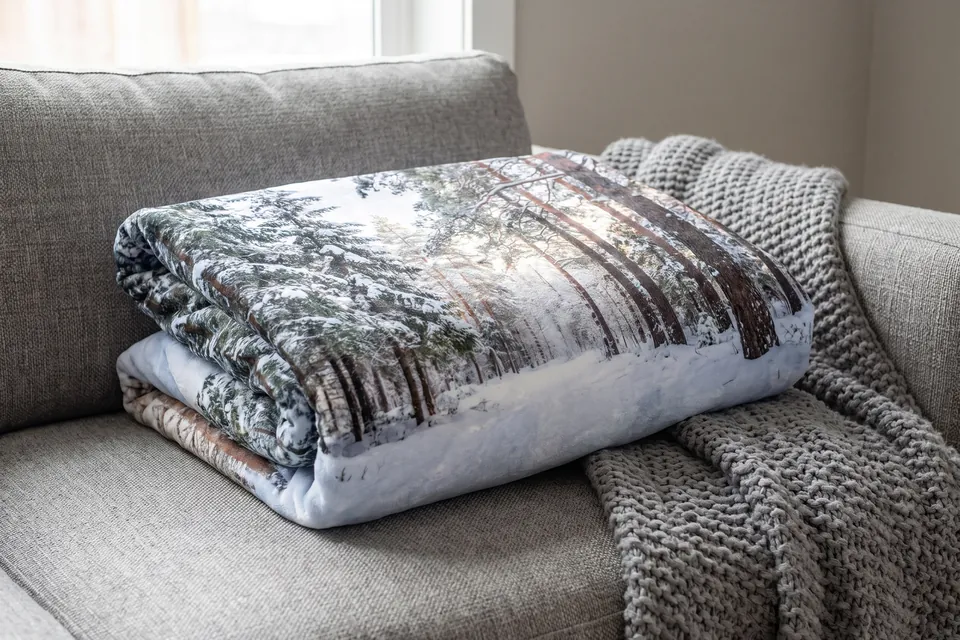 Fotodecke mit Winterwald neben einer Strickdecke auf einem Sofa
