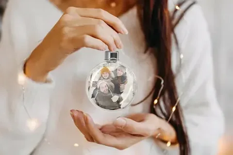 Hand hält eine Christbaumkugel mit eigenem Foto