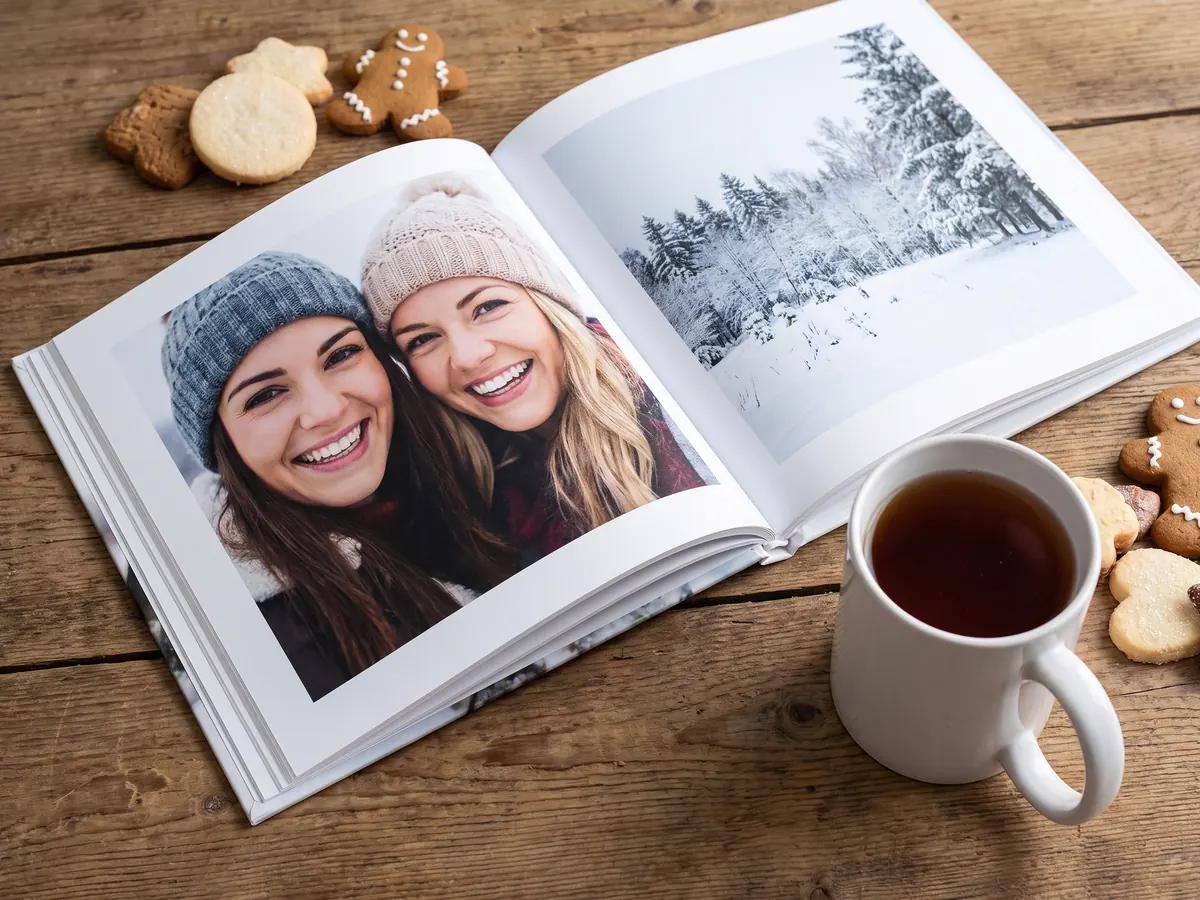 Weihnachtsfotobuch mit Fotos von zwei Freundinnen neben Tee und Plätzchen